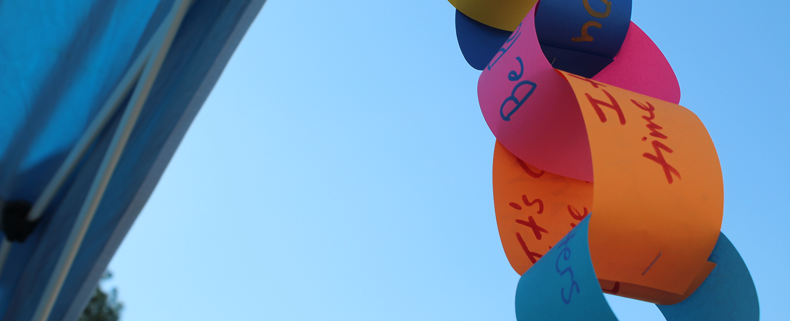 A paper chain with positive notes written on them with the sky in the background
