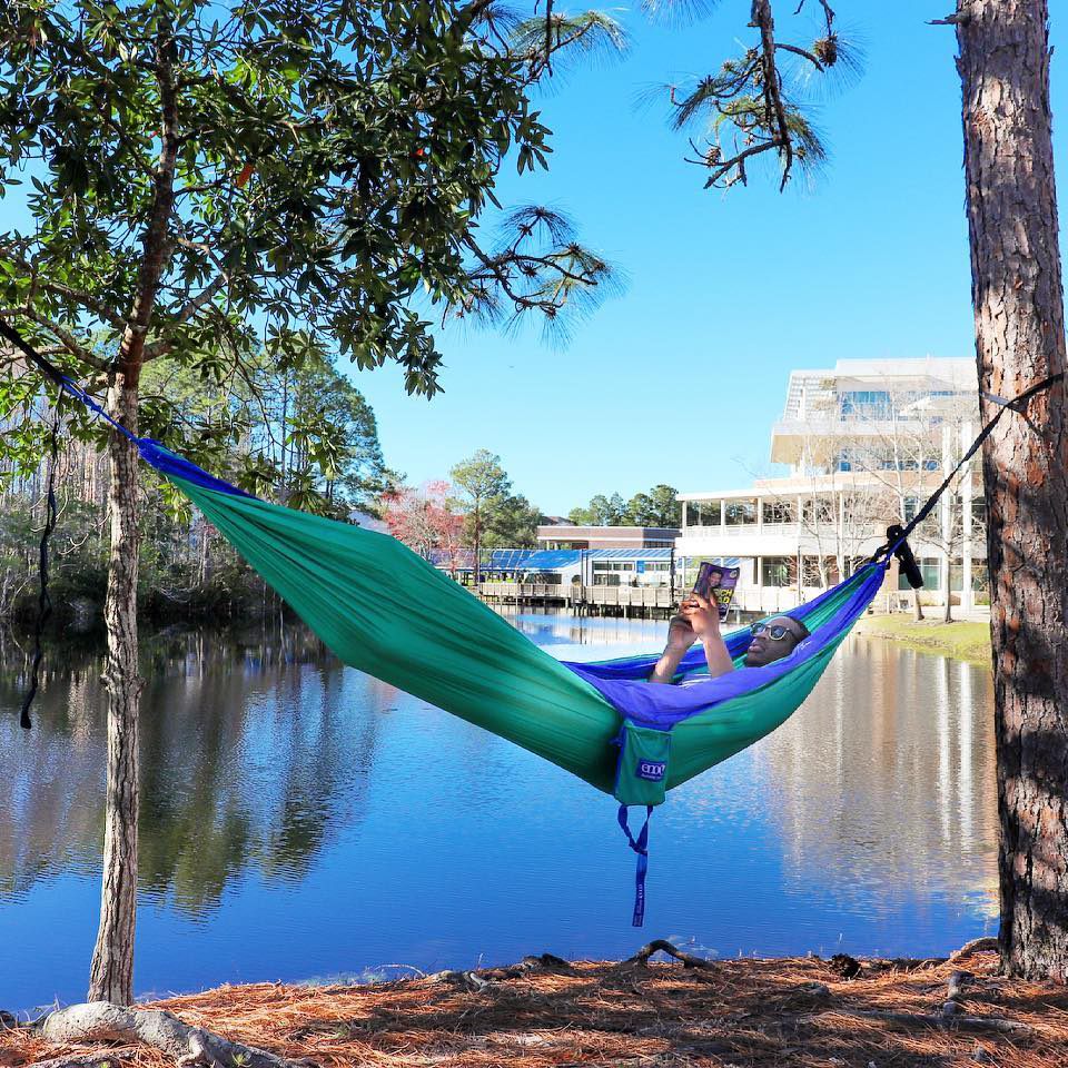 resident reading a book in a hammock outside of osprey landing and osprey hall on a sunny day