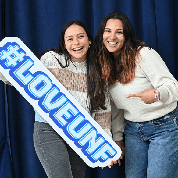 Two UNF student smiling and holding a hashtag Love UNF Sign