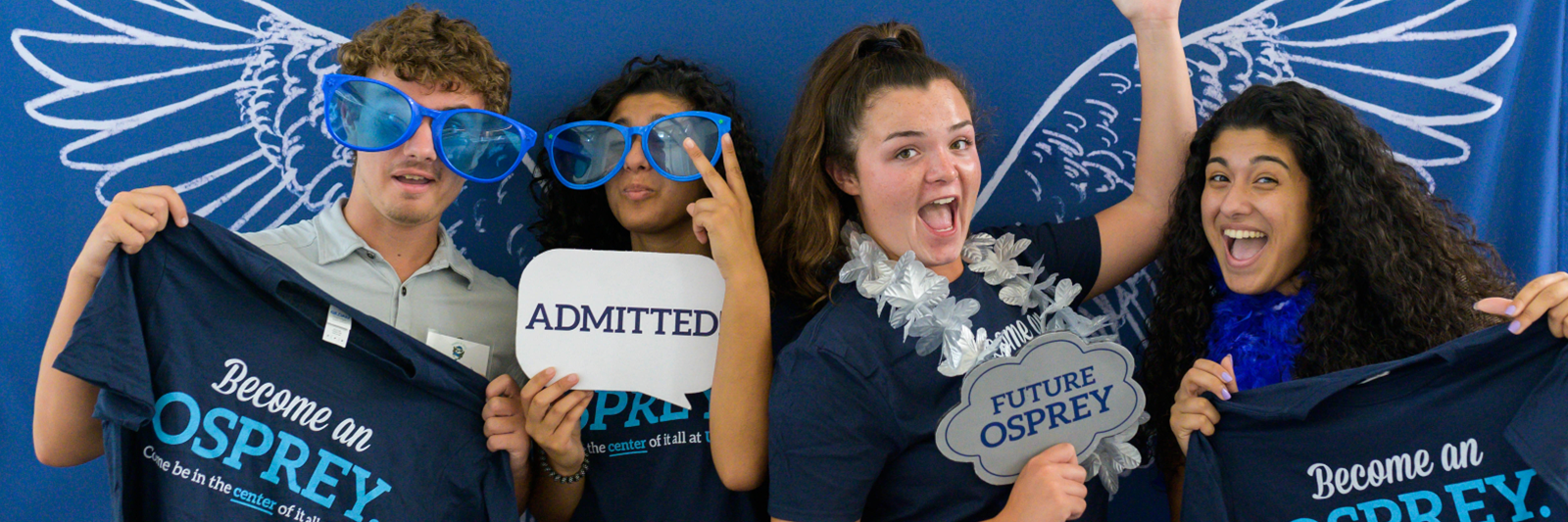 Four new UNF students in a photo booth holding UNF signs and striking fun poses