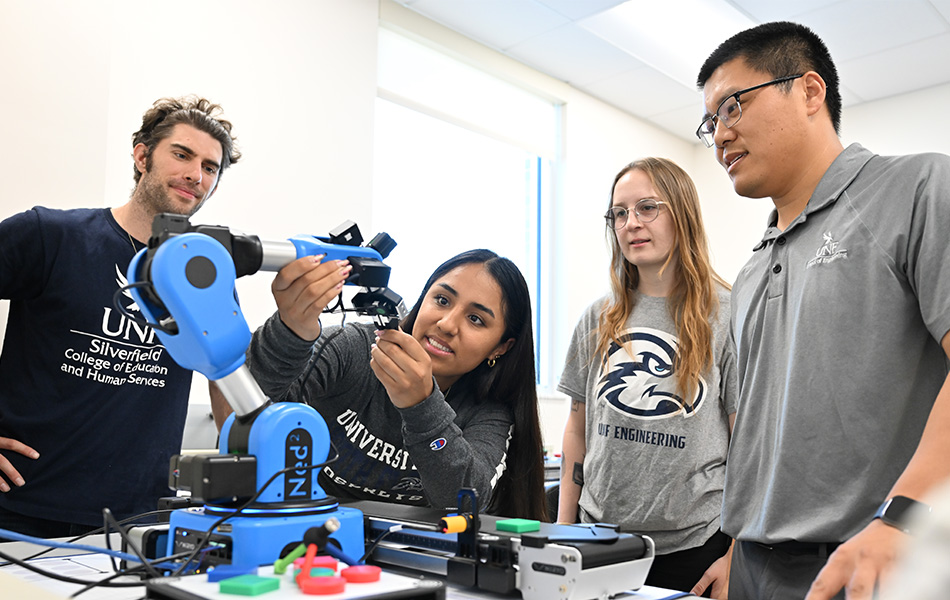 students and a professor working together to fix a manufacturing device