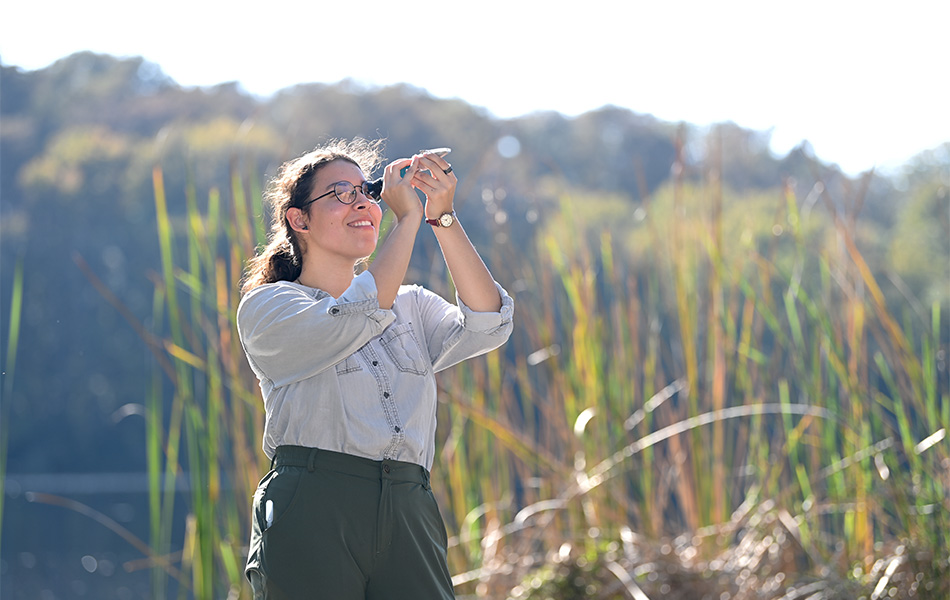student using a microscope to examine a shell while standing in a wetland