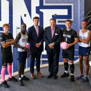 Six men stand in front of a "UNF" sign wearing pink for Breast Cancer Awareness