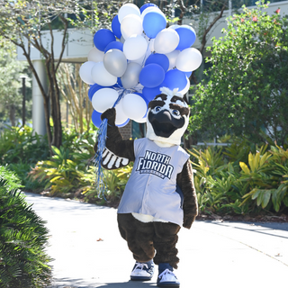 Ozzie the mascot holding blue, white, and gray ballons