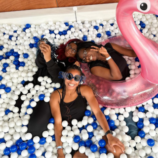 Three students smile and look up at camera, surrounded by blue and white balls in a ball pit