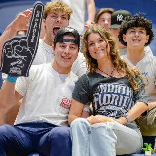 four people smiling and one person holding up a blue foam finger that says "Go Ospreys"