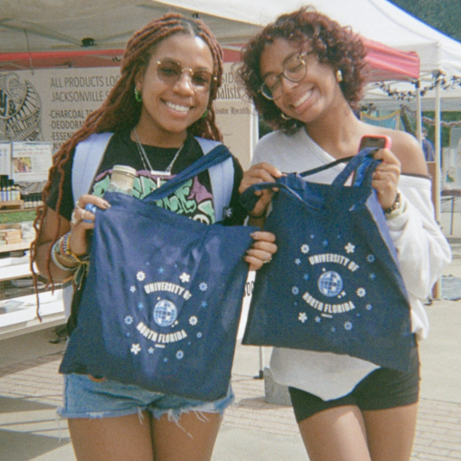 Two girls stand holding handbags that say "University of North Florida"
