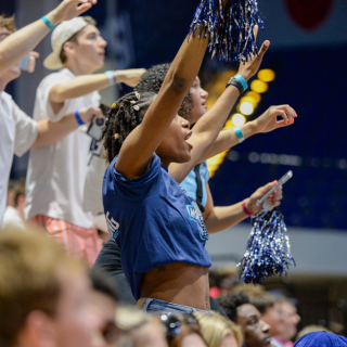 Student cheering at basketball game with blue pompoms in hand