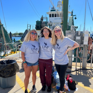 Three students smile in front of a boat