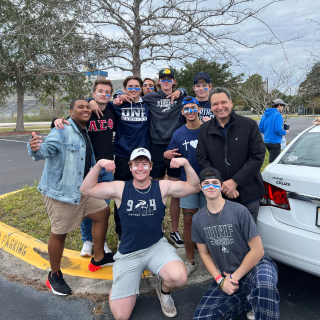 A group standing outside poses for a picture at a tailgate