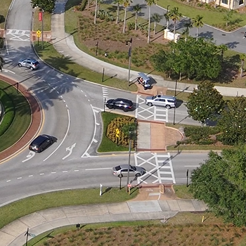 birds eye view of a roundabout with a golf cart waiting to cross as cars enter the circle