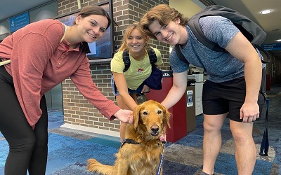 Three students smile while petting a golden retriever wearing a Campus Canines vest