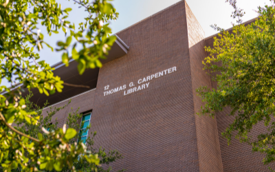 sign with 12 Thomas G. Carpenter Library on a brick building exterior framed by tree branches
