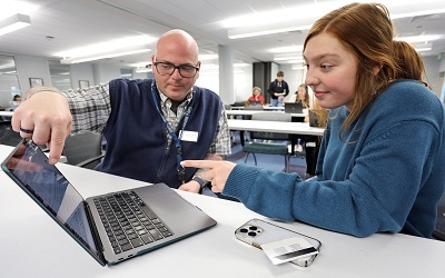 a librarian pointing to a laptop screen while assisting a student
