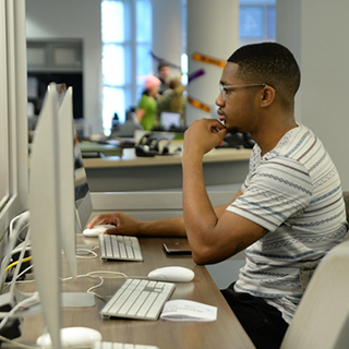 student sitting at a mac computer in library