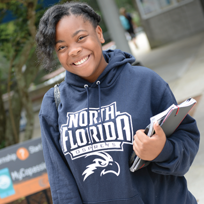 Student in UNF hoodie holding notebooks