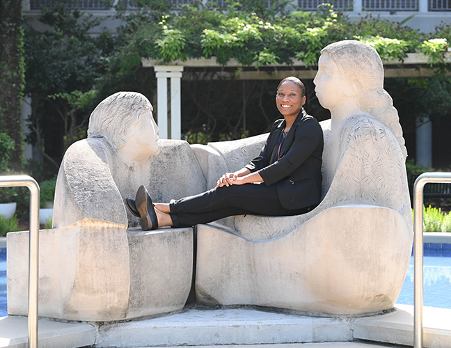 Asia Bell sitting on the statue outside Brooks College of Health