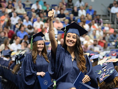 student holding up a thumbs up at graduation