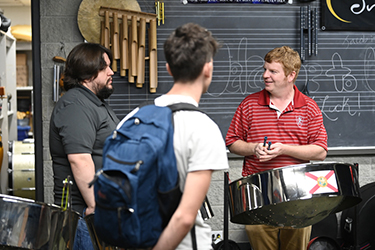 Shaun Bennett standing by a steel drum talking with two students