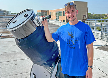UNF student standing on a roof next to a microscope