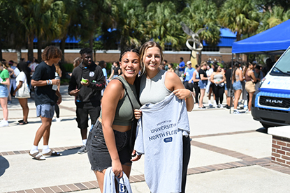 Two UNF students hanging out in Osprey Plaza with T-shirts in their hands