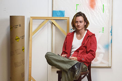 Brennan Wojtyla sitting in a chair next to his artwork