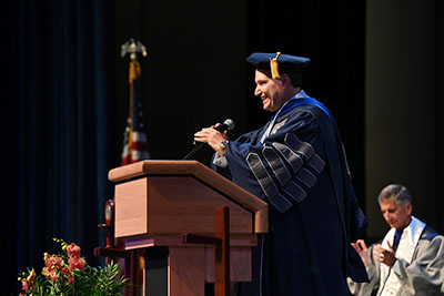President Limayem speaking at a podium wearing a gown