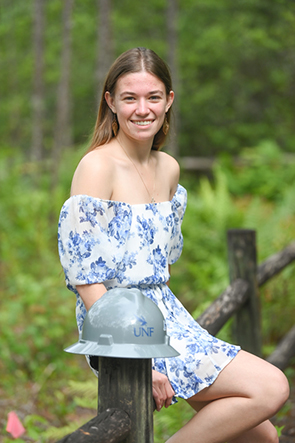 Emily Rossello sitting on a wood fence with a UNF construction hat