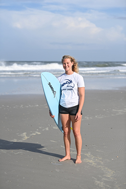 Female UNF surfer standing on the beach with a surfboard