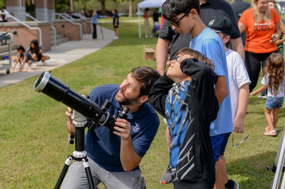 Children and UNF professor looking up at solar eclipse with a telescope