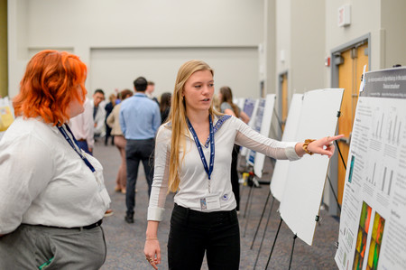 UNF student pointing to her research poster at the 2024 SOARS Symposium