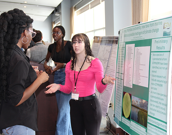 Student in pink shirt explaining her research poster to an onlooker