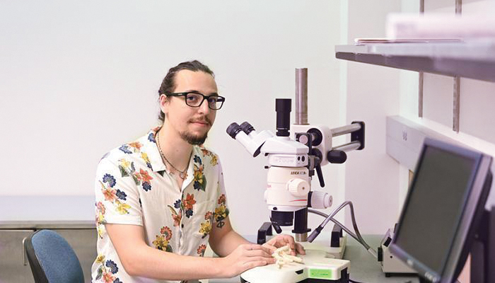 UNF alum Corey Kempinski sitting in front of a microscope