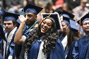 UNF female grad smiling and waving at the fall 2024 commencement