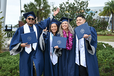 Four UNF grads smiling and posing with their diplomas