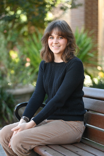 UNF student Victoria (Vic) Hayes sitting on a bench on the UNF campus