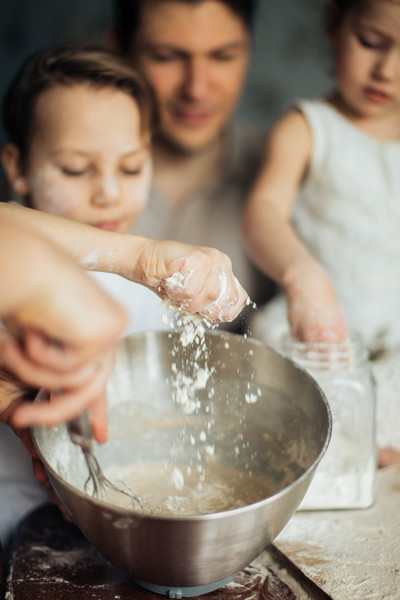 Hands dropping flour into a whisking bowl