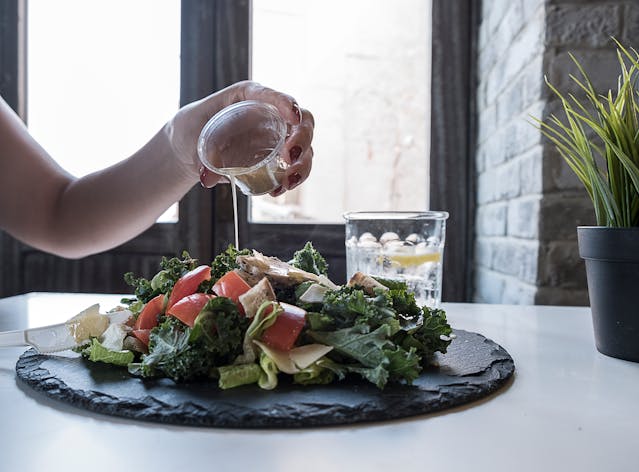 hand pouring dressing on a kale salad