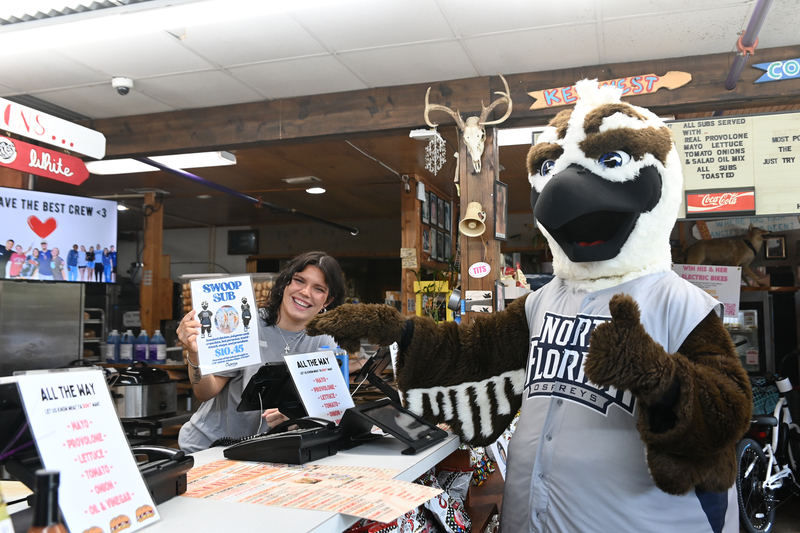 Ozzie the Mascot at Angie's Subs conversing with an employee holding a "Swoop Sub" sign