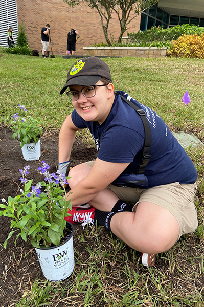 UNF Swoop Into Service volunteer sitting with legs crossed while planting plants in the ground