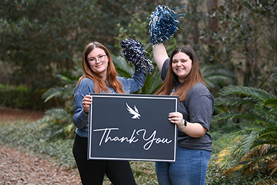 Two female UNF students holding a Thank You sign and pom poms