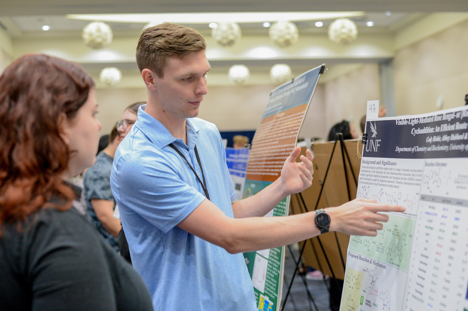 Student pointing to a poster discussing his research to onlookers