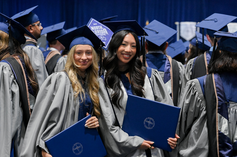 Graduates at commencement posing with their diploma booklets