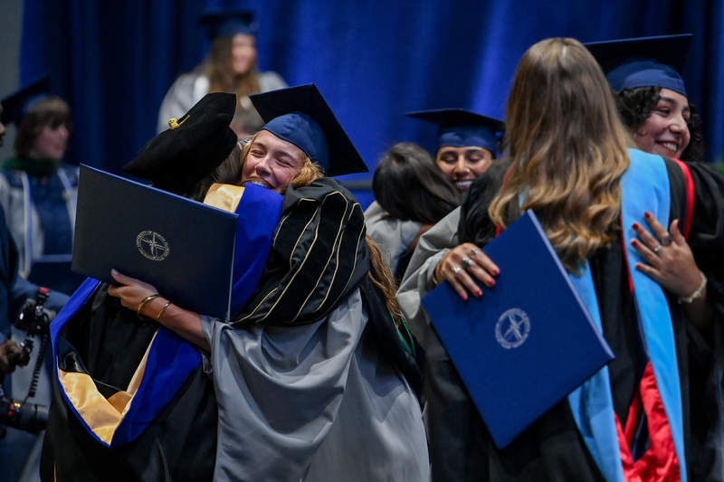 Graduates at commencement hugging faculty members