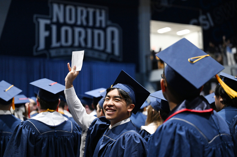 Male UNF graduate at commencement waving at the audience