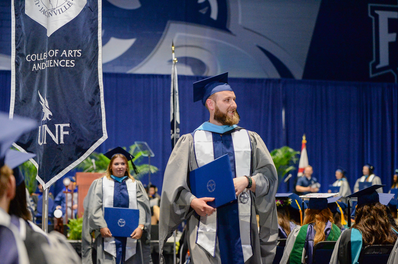 UNF graduate walking down the aisle holding his diploma