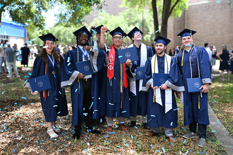 UNF graduates in cap and gowns outside celebrating with confetti