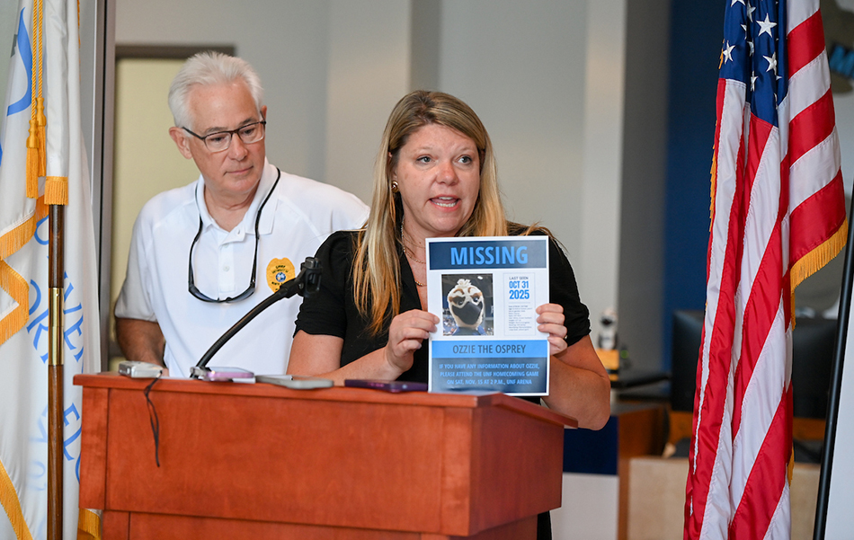 Andrea Jones (VP of UNF Marcomm) at a podium holding a flyer