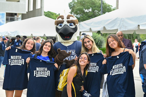 Ozzie standing with students holding up UNF t-shirts