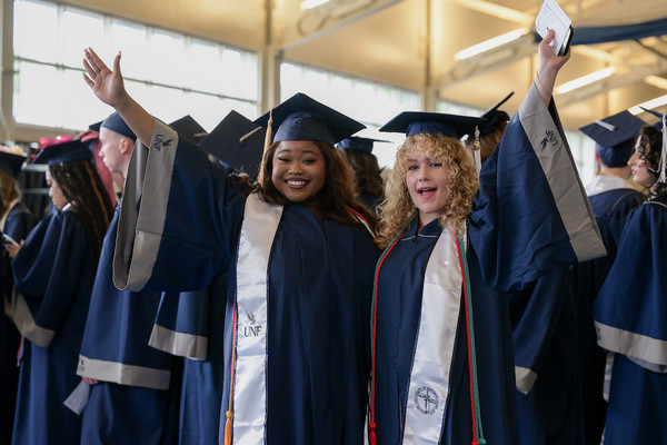 Two female UNF students at graduation in cap and gown waving